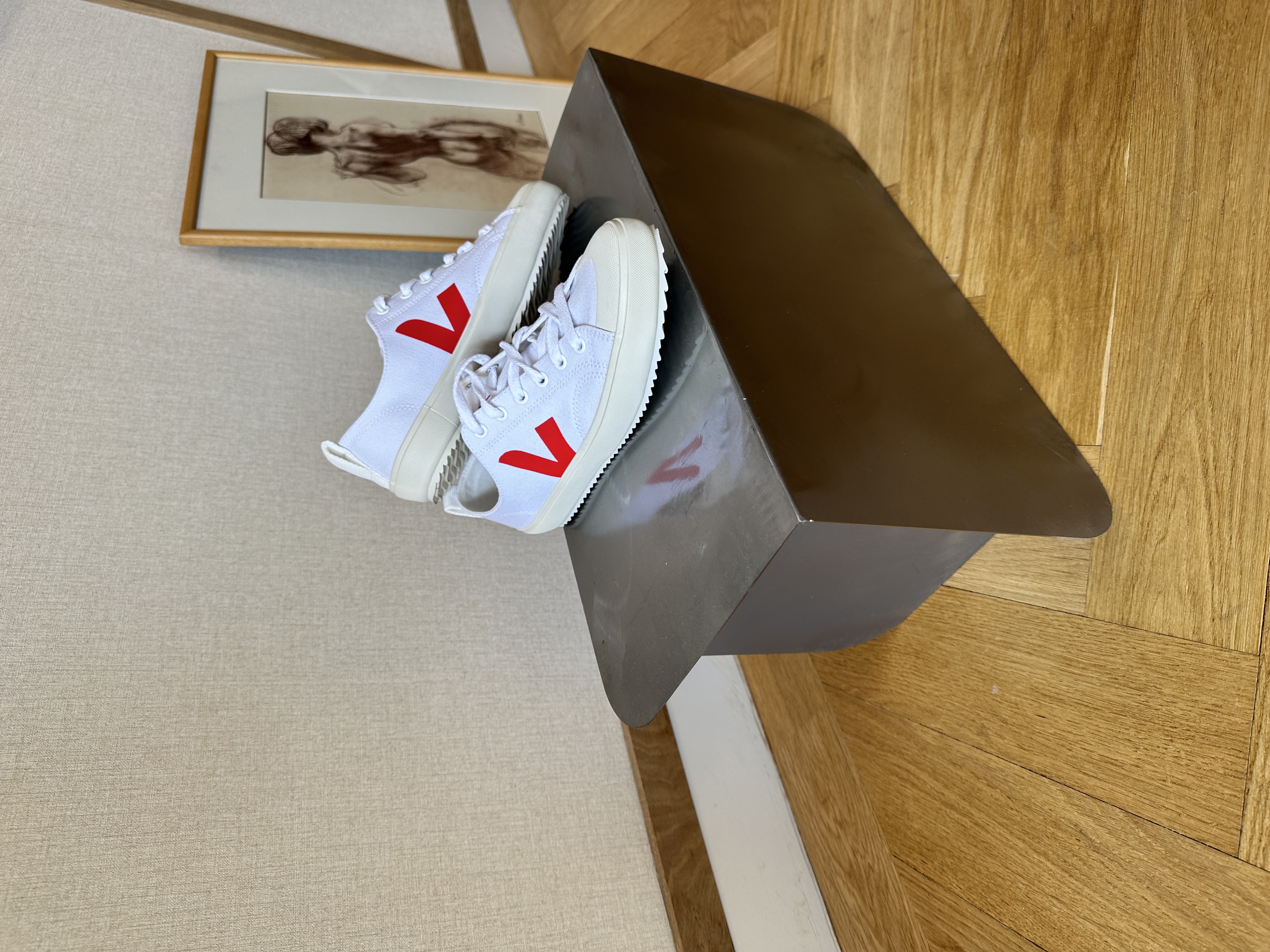 Maatwerk schoenenstand in onbehandeld staal met witte sneakers — minimalistische retailpresentatie voor duurzaam modemerk